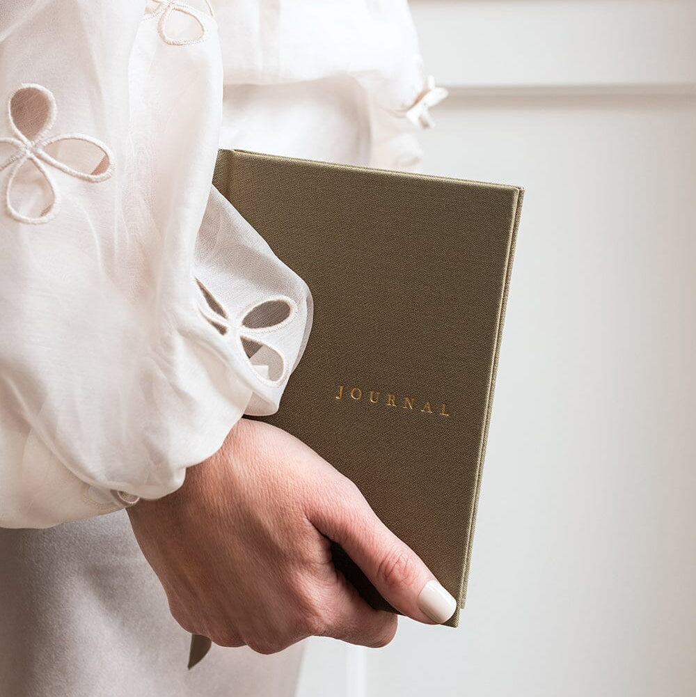 Person holding a brown journal with 'JOURNAL' written on it, wearing a white blouse.