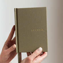 Hand holding a green journal with 'JOURNAL' embossed on it against a light background