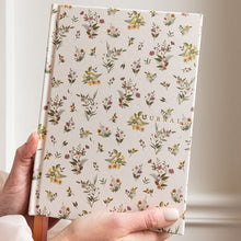 Hand holding a floral-patterned journal against a neutral background