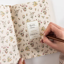 Floral notebook with a hand holding a pen on a white background