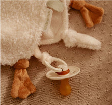Fluffy white goose toy with a white pacifier attached on a textured brown surface.
