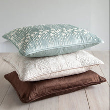 Three decorative pillows in blue, beige, and brown on a light wooden floor.