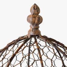 Close-up of a rustic metal birdcage top featuring a textured, weathered bronze finial and a woven wire dome structure on a plain white background.