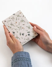 Hands holding a small notebook with a floral pattern on a white background