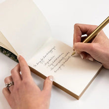 Person writing in a notebook with a pen on a white surface