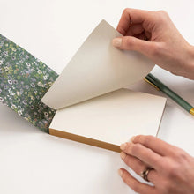 Person holding a floral-patterned book with a pencil on a white background