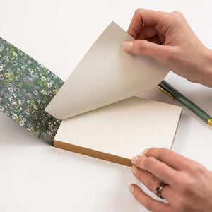 Person holding a floral-patterned book with a pencil on a white background