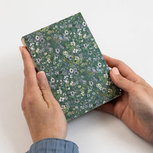Person holding a small floral notebook on a white background