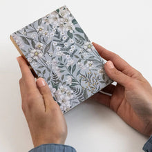 Person holding a small notebook with floral design on a white background