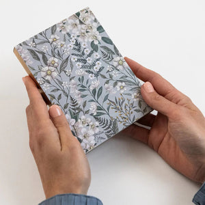 Person holding a small notebook with floral design on a white background