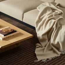 Beige blanket draped over a beige sofa next to a wooden coffee table with decorative items.