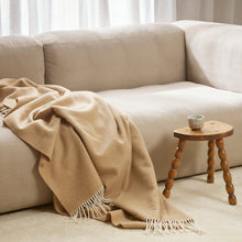 Beige blanket draped over a beige sofa with a wooden side table in a living room setting.