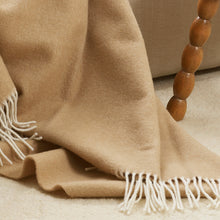 Beige blanket with white fringes draped over a wooden chair.