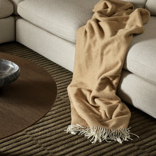 Beige blanket draped over a beige sofa with a dark coffee table in the foreground.
