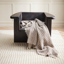 Black armchair with a gray blanket draped over it in a room with wooden flooring and paneled walls.