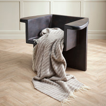 Modern black chair with a gray blanket draped over it on a wooden floor.