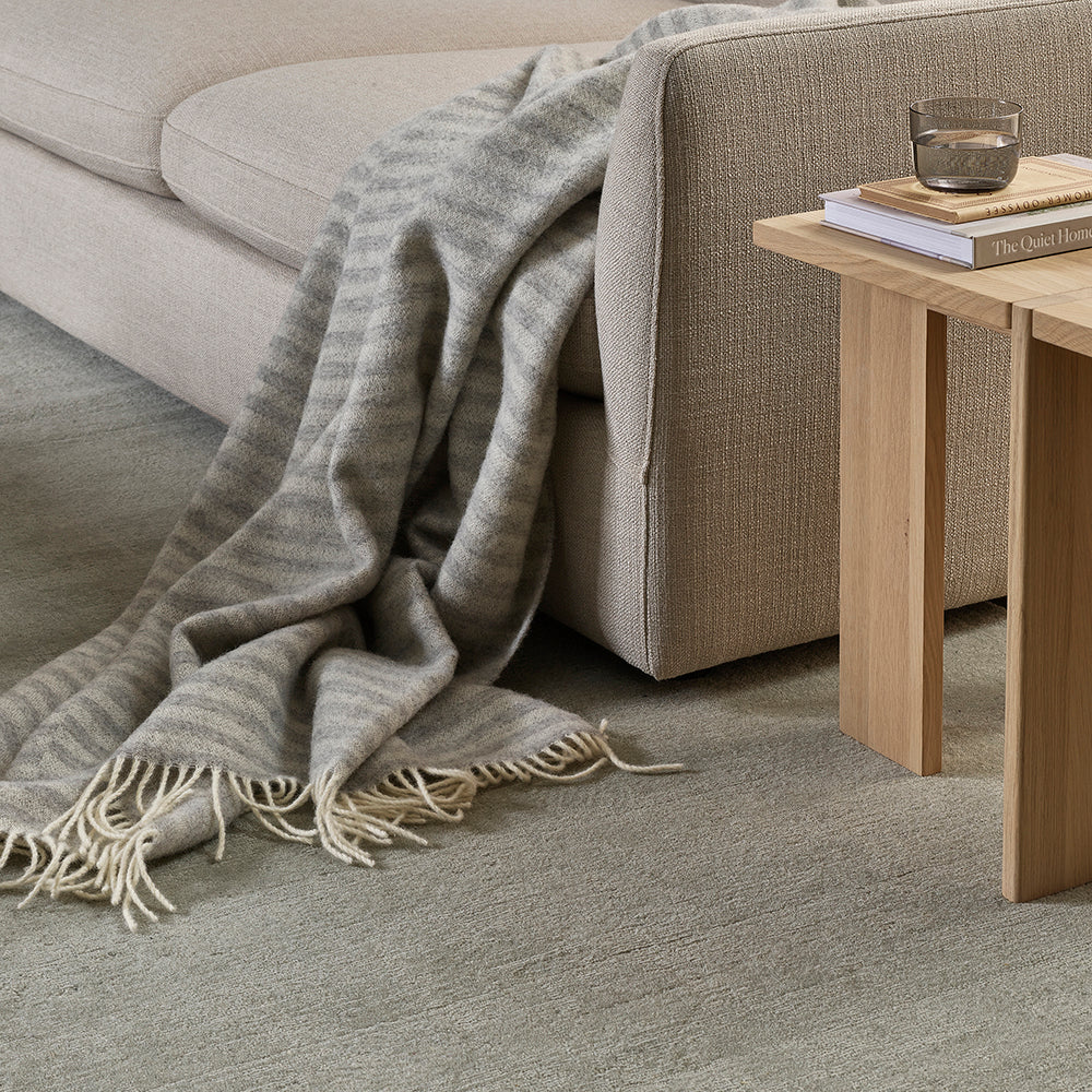 Gray textured carpet with a blanket draped over a sofa and a wooden side table.