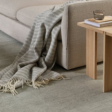 Gray textured carpet with a blanket draped over a sofa and a wooden side table.