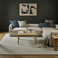 Modern living room with a beige sectional sofa, abstract art on the wall, and wooden coffee table.