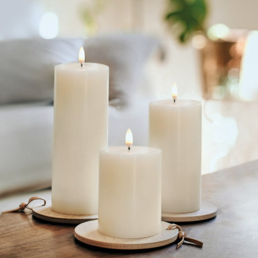 Three lit white pillar candles on wooden coasters