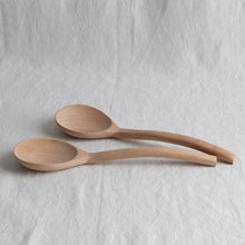 Two wooden salad spoons on a light gray textured surface

