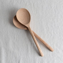 Two wooden salad spoons on a light gray textured surface


