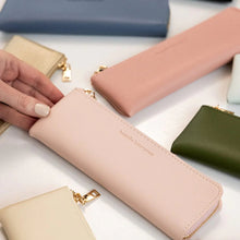 Collection of colorful pencil cases on a white surface with a hand interacting with one.