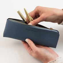 Person holding a blue pencil case with gold pens on a white background