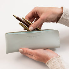 Hand holding a light blue pencil case with gold pens on a white background