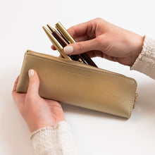 Gold pencil case with pens held by a hand on a white background