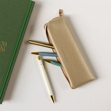 Green notebook, gold pencil case, and pens on a light background
