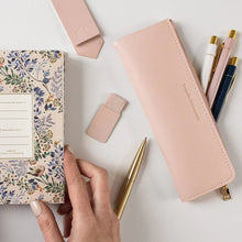 Pink pen holder with pens, a notebook, and a small pouch on a light surface.