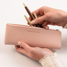 Person holding a pink pencil case with gold pens on a white background