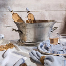 Two bottles of wine in a metal ice bucket on a table with glasses and napkins.