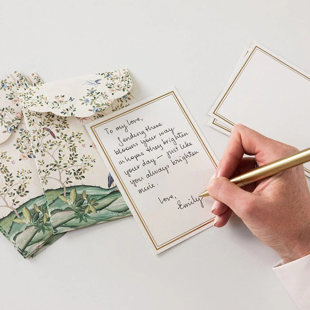Hand writing on a card with floral stationery items on a light surface