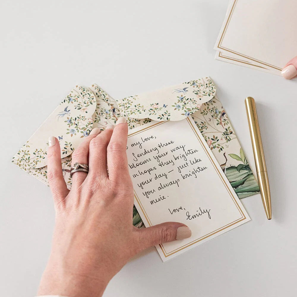 Handwritten letter on a floral card with a gold pen on a light surface