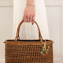 Brown woven handbag with a keychain held by a person wearing a white dress.