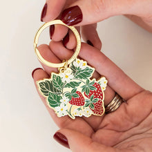 Hand holding a keychain with strawberry design against a white background