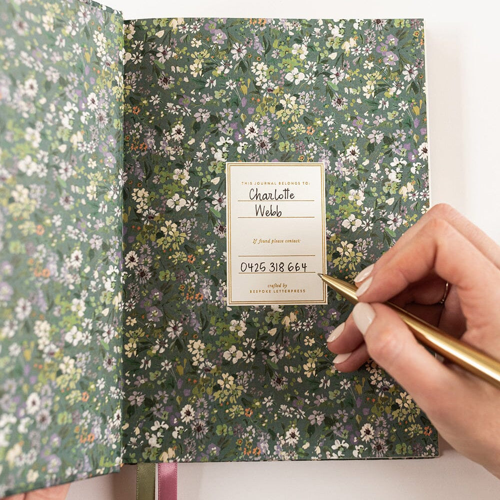 Floral notebook with a gold pen and name card on a white background