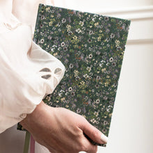 Hand holding a floral-patterned notebook with a white blouse in the background