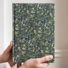 Hand holding a floral notebook against a neutral background