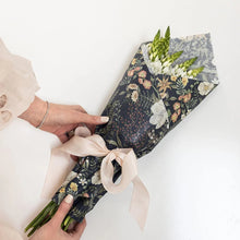 Bouquet of flowers wrapped in decorative paper with a person holding it on a white background