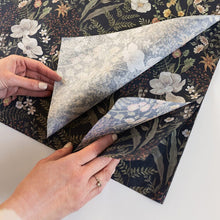 Hands folding floral-patterned paper with a dark background