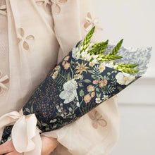 Floral-patterned wrapping paper with flowers held by a person wearing a beige garment.