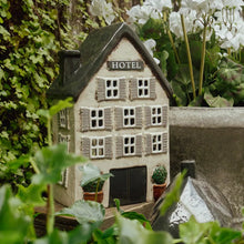 Miniature model of a hotel surrounded by greenery and white flowers.  Used for tea light candle.