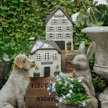 Decorative miniature house with 'Patisserie' sign, surrounded by garden elements including stone dog, rabbit and plants.