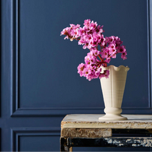 White vase with pink flowers on a wooden table against a blue wall