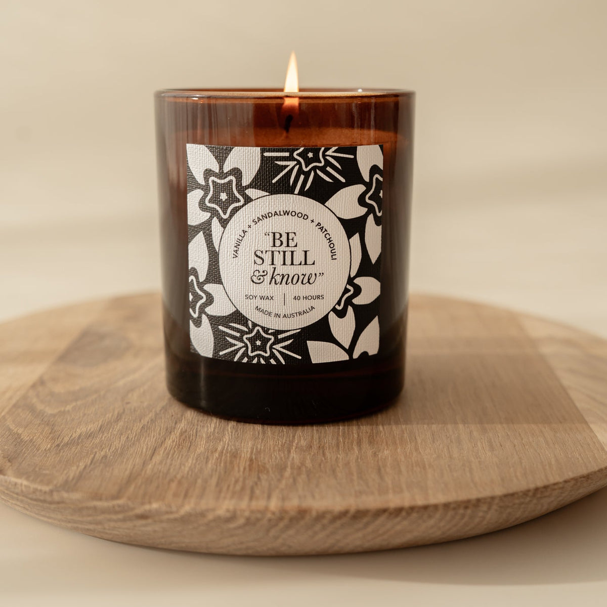Well Versed Homes Signature Candle with label that says 'be still and know' sitting on a wooden board