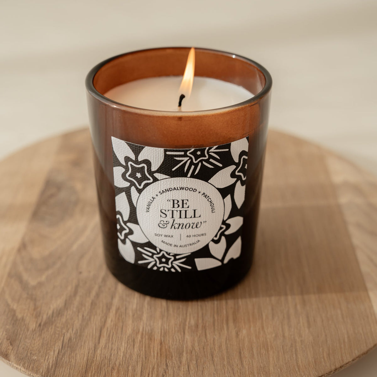 Well Versed Homes Signature Candle with label that says 'be still and know' sitting on a wooden board