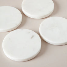 Four white marble coasters on a beige surface